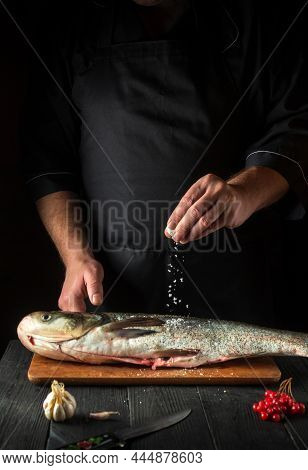 The Chef Prepares Silver Carp Herring In The Restaurant Kitchen. The Cook Sprinkles Salt On The Fish