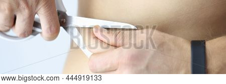 Man Cuts Off Excess Skin With Fat From Abdomen With Scissors. Diet And Weight Loss Concept