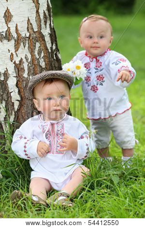 Little boy and girl in russian folk costumes near the birch in park