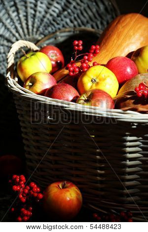 Juicy apples and pumpkin in wooden basket on table close-up