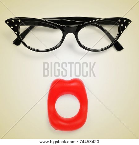 a pair of glasses and a fake mouth forming a woman face on a beige background, with a retro effect