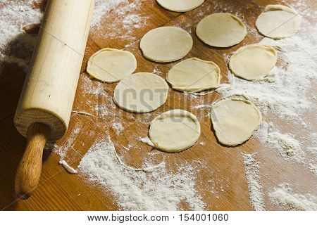 Circles of dough and rolling pin on the wooden table. Homemade process of preparation Russian Belarussian Ukrainian meals 