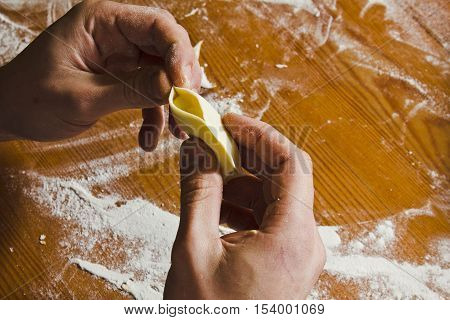Male shapes dumplings with potatoes on the wooden table. Homemade process of preparation Russian Belarussian Ukrainian meals "vareniki" (it can be used for dumplings ravioli tortellini as well). Hands close-up.