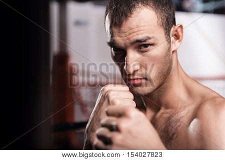 Ready to fight. Close up portrait of young-looking handsome man holding boxing position while looking forward.