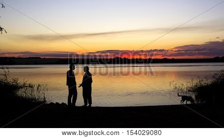 two men are talking and dog is walking