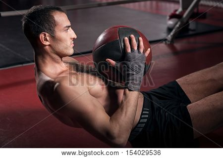 Intense workout. Young brawny man doing some abdominal crunches on floor with help of special fitness ball.
