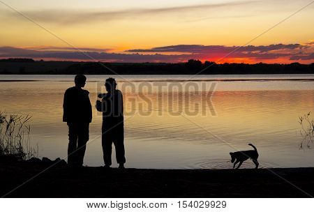 two men are talking and dog is walking