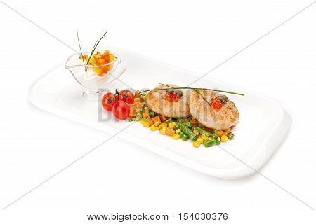 The dietary fish cutlets served on a white dish with a garnish from corn and asparagus haricot, with sauce, decorated by red caviar,  isolated on a white background.