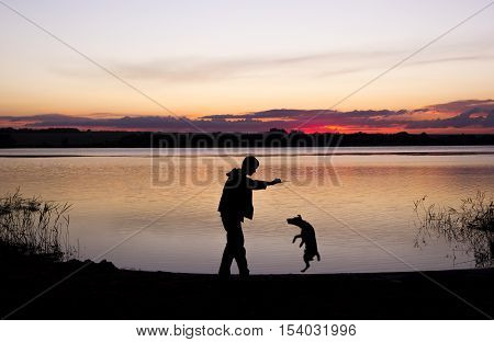 boy is playing with dog at lake during sunset