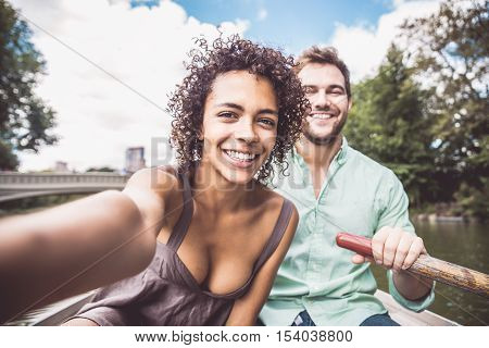 Happy couple having fun on a boat in Central Park - Interracial couple taking a selfie while sightseeing Manhattan
