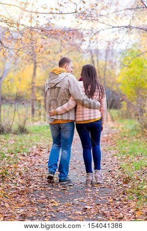 smiling couple hugging in autumn park from back on the road between the trees