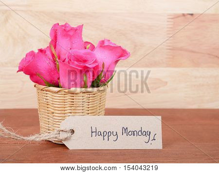 Pink rose flower in the basket and handwriting Happy Monday brown label with wood background