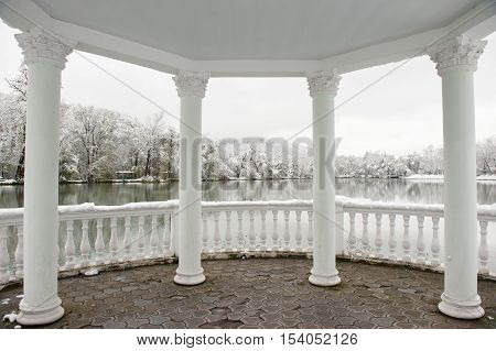 white gazebo with roof and columns on a background of winter landscape with lake