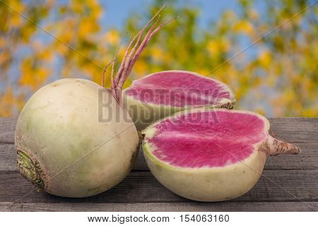 One whole and sliced watermelon radish on a wooden table with blurred garden background.