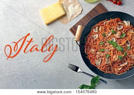 Pan with delicious pasta on wooden cutting board. Word ITALY on gray background. Italian food concept.