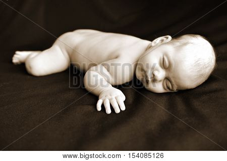 A newborn baby sleeps on a black blanket in peace.