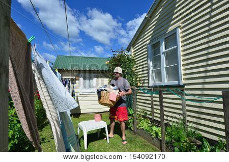 A young smiling man drinks beer while hanging clothes on clothes line using clothes peg.