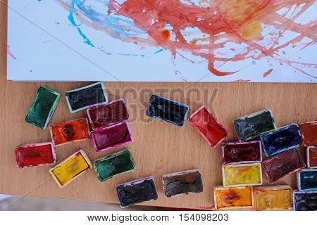 Top view of watercolor containers and album with abstract preschooler's drawings.