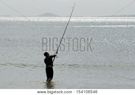Young man fishing with a surfcaster on a seashore.