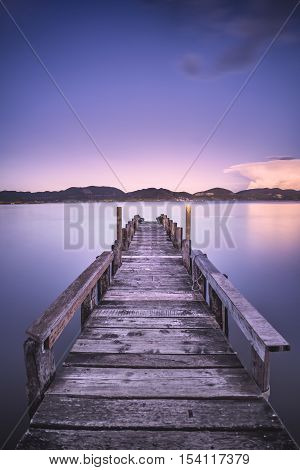 Wooden pier or jetty on blue lake sunset and sky reflection water. Long exposure Versilia Massaciuccoli Tuscany Italy.