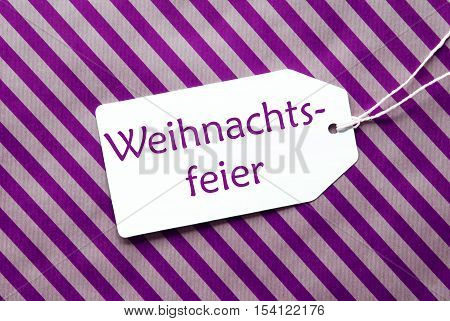 German Text Weihnachtsfeier Means Christmas Party. One Label On A Purple Striped Wrapping Paper. Textured Background. Tag With Ribbon.
