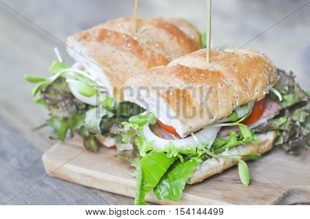 baguette sandwich with ham tomato and lettuce on wooden plate