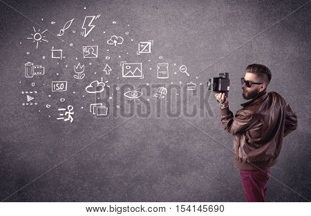 An elegant hipster guy trying to use a vintage camera with camera settings icons drawn on wall, like flash, white balace or ISO value concept