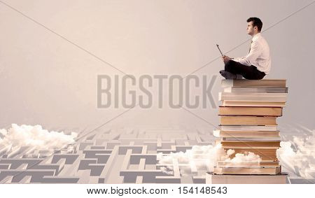 A businessman with laptop tablet in elegant suit sitting on a stack of books on top of sandy labirynth background concept