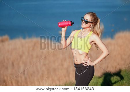 Beautiful fitness blonde girl stopped to drink water after the running. sport and work out girl in sunny day