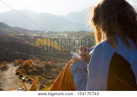 Female traveler writing her thoughts at sunset. Adventurer sitting down with pen and book.