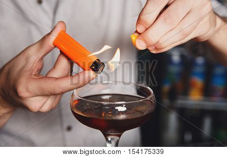 Barman's hands in bar interior making alcohol flaming cocktail. Professional bartender at work in bar mixing drink with burning fire. Party time in night club