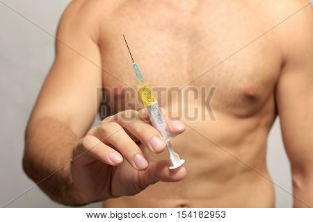 Muscular man holding syringe, closeup