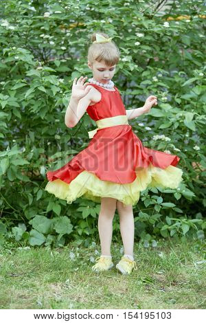 Little girl dressed in red gown with yellow underskirt spins standing outdoor.
