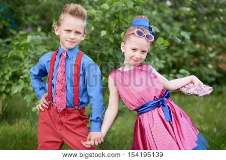 Boy and girl dressed in red and blue costumes pose at grassy lawn.