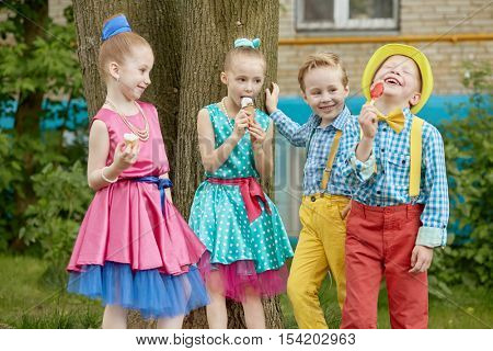 Four children stand outdoot on summer day. Three of them eat icecream, one boy laughs.