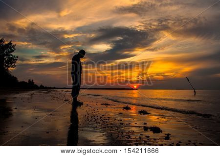 Silhouette of sad man in the beach during sunset in the background. Far away concept. Alone & lonely concept.