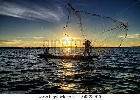 Silhouette fisherman trowing the net at the lake before sunset countryside of Thailand