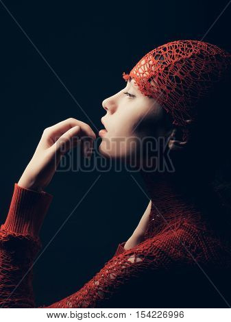 sexy young woman or cute girl with tender arm arm touch lips and pretty natural face profile wrapped in red knitted fashionable shirt on dark background
