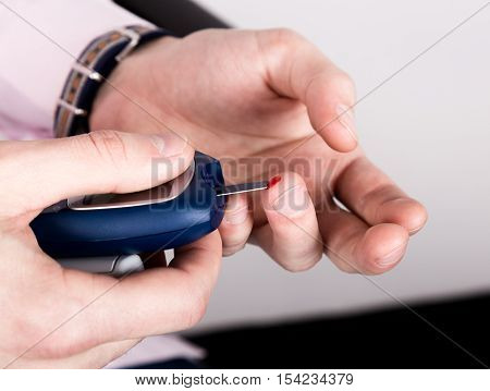 Dependent first type diabetes patient. Measuring glucose level blood test using ultra mini glucometer and small drop of blood from finger and test strips.