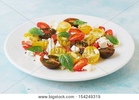 Summer heirloom tomato salad with fresh feta cheese on white plate on blue background selective focus horizontal