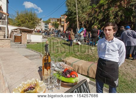 TBILISI, GEORGIA - OCT 16, 2016: Young man invites tourists for tasting Chacha traditional alcoholic drink at city festival Tbilisoba on October 16, 2016. Tbilisoba is a festival in Tbilisi from 1979