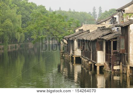 Wooden weathered buildings lining the water canals in tongxiang wuzhen scenic town east view in Zhejiang province China in the early morning mist.