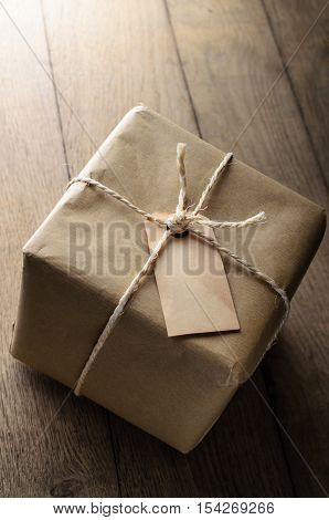 A string tied parcel wrapped in brown paper with old weathered blank label for copy space. Set on oak planking to represent table or floor.