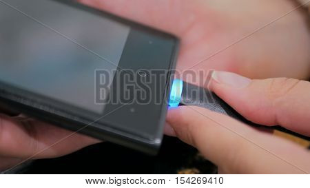 Woman's hand plugging black lightning charging cable into smartphone - USB data cable connecting on modern gadget. Close up