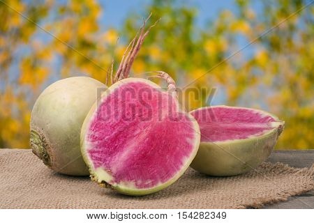 One whole and sliced watermelon radish on a wooden table with blurred garden background.