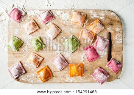 Multi-colored ravioli on a cutting board, sprinkled with flour, cooking process, on a white table. Funny food for children. View from above