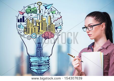 Thoughtful young businesswoman and creative light bulb with financial sketch on blurry city background. Business idea concept