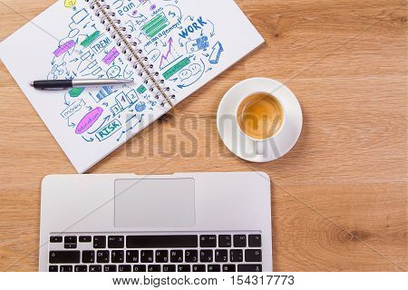 Top view of wooden office desktop with business sketch in spiral notepad coffee cup and laptop keyboard