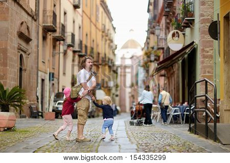 Two little sisters and their father on a street of typical italian town