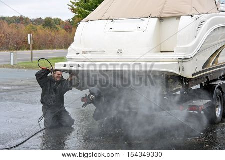 Caucasian man cleaning underside of power boat with pressure washer